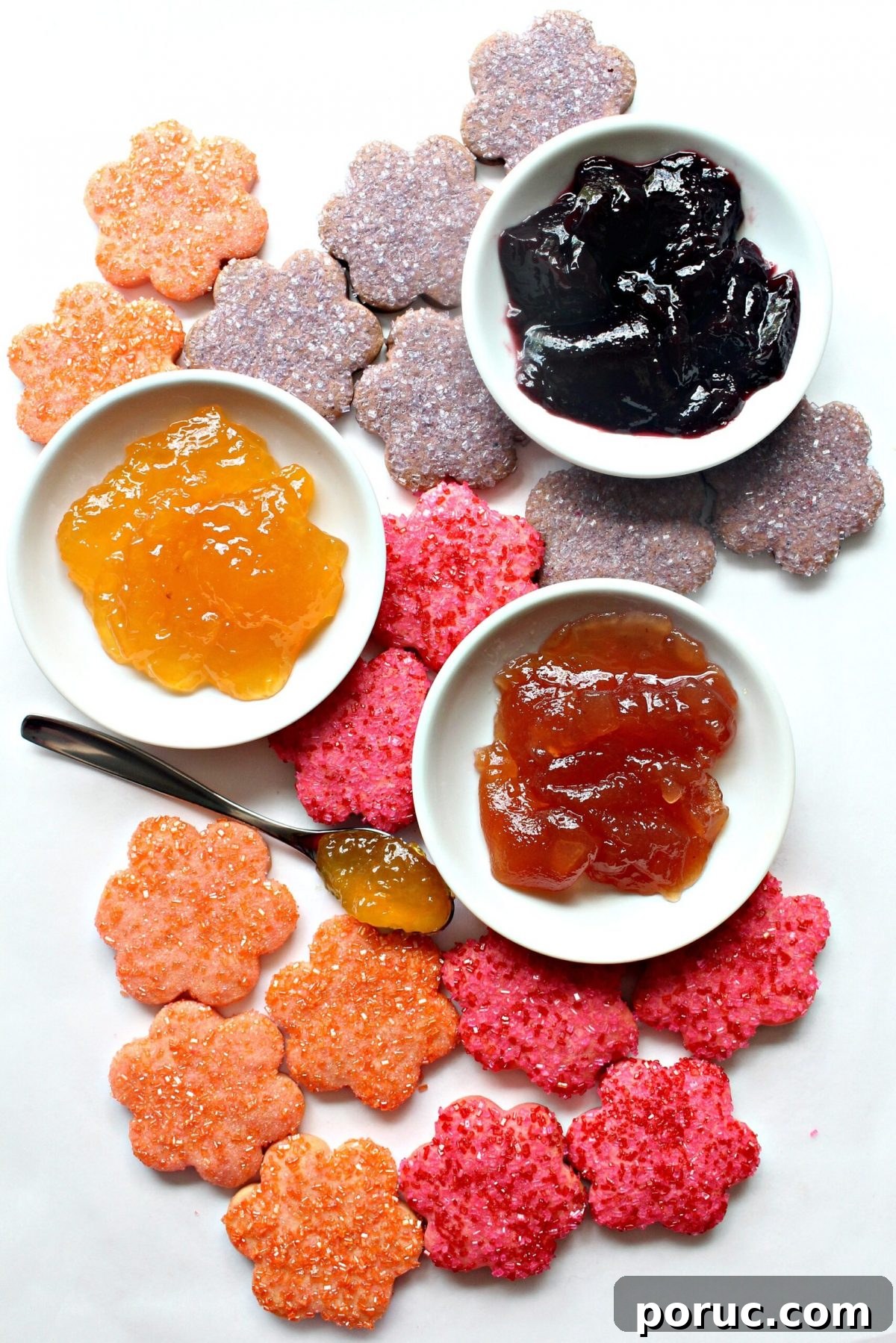 Jam-Filled Butter Cookies Recipe: Crispy, Buttery Thumbprints 2 Jam Butter cookies cut out in flower shapes, colored orange, pink, or purple.