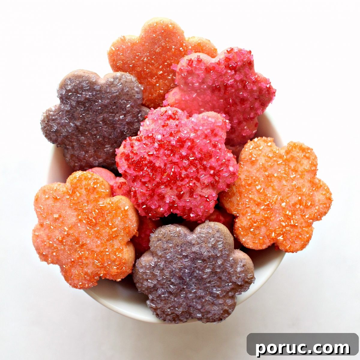 Jam-Filled Butter Cookies Recipe: Crispy, Buttery Thumbprints 3 A bowl filled with orange, pink, and purple cookies cut out in daisy shapes.