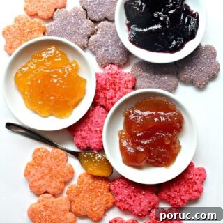 Jam-Filled Butter Cookies Recipe: Crispy, Buttery Thumbprints 7 Jam Butter cookies cut out in flower shapes, colored orange, pink, or purple.