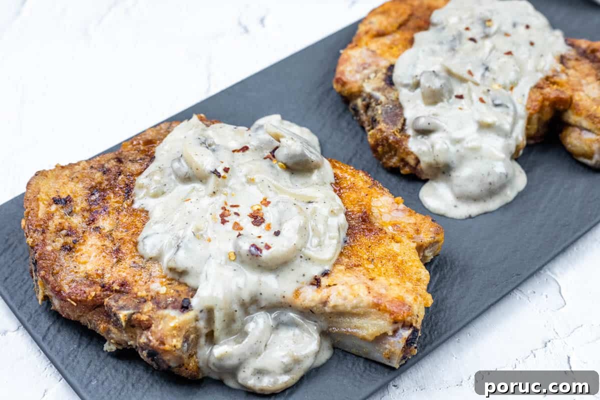 25 Comfort-Food Recipes That Satisfy Every Craving 2 Two Smothered Pork Chops with Onions & Mushrooms on a black rectangular plate.