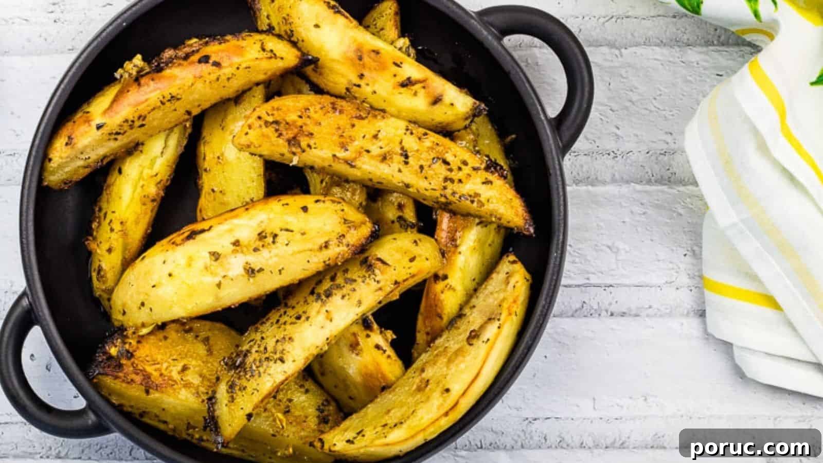 25 Comfort-Food Recipes That Satisfy Every Craving 16 Round black dish filled with seasoned roasted potato wedges, placed on a white wooden surface alongside a white and yellow striped cloth napkin.