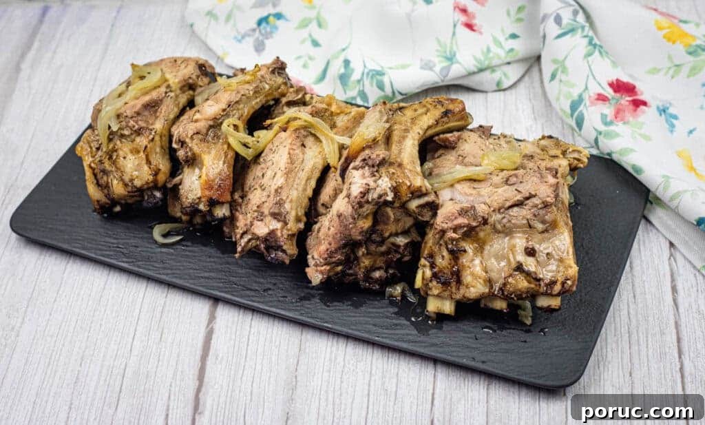 25 Comfort-Food Recipes That Satisfy Every Craving 22 Oven Baked Ribs with cooked onions on a black rectangular slate platter, set on a wooden surface. A floral-patterned cloth is partially visible in the background.