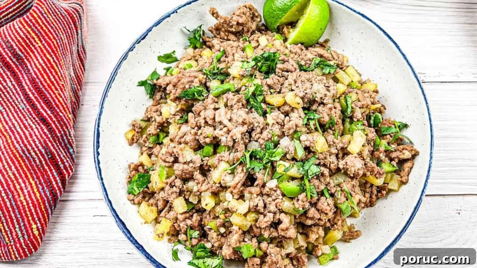 25 Comfort-Food Recipes That Satisfy Every Craving 27 A plate of cooked ground beef mixed with diced vegetables and garnished with lime wedges and chopped herbs. A red striped cloth is placed beside the plate.