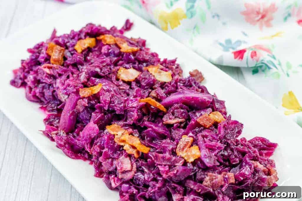 25 Comfort-Food Recipes That Satisfy Every Craving 4 A rectangular white plate with cooked red cabbage and bacon pieces, placed on a light surface next to a floral-patterned cloth.