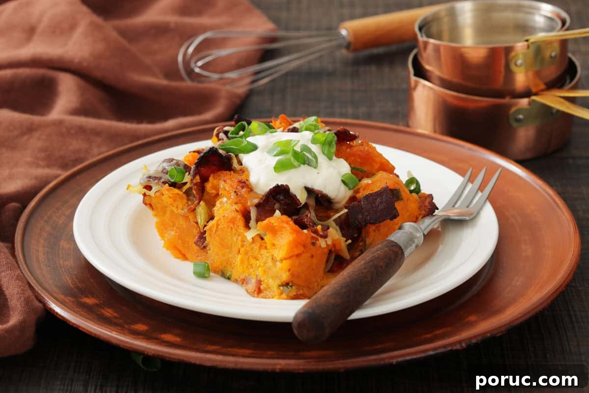 25 Comfort-Food Recipes That Satisfy Every Craving 7 A white plate with loaded sweet potato casserole topped with sour cream, bacon, cheese, and green onions, set on a brown charger plate with a fork and cooking utensils in the background.