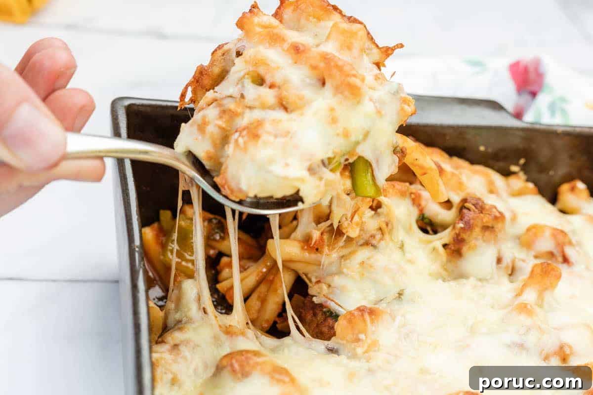 25 Comfort-Food Recipes That Satisfy Every Craving 9 A hand lifts a serving of meatball casserole from a rectangular baking dish, showing melted cheese stretching.