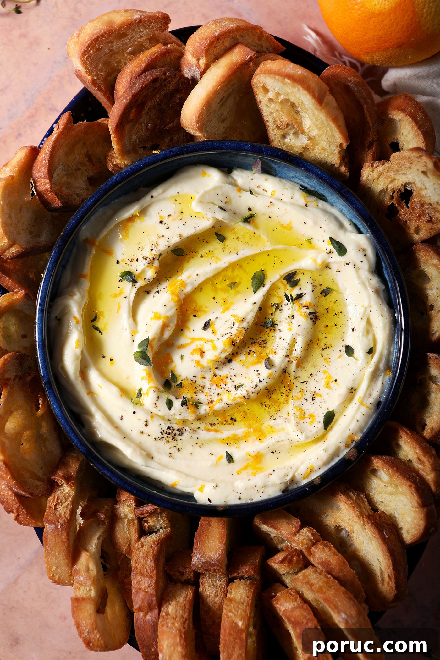 Creamy Whipped Ricotta Dip with Lemon and Herbs 2 A bowl of whipped ricotta dip garnished with extra thyme, orange zest and olive oil surrounded by crostini on a terracotta surface