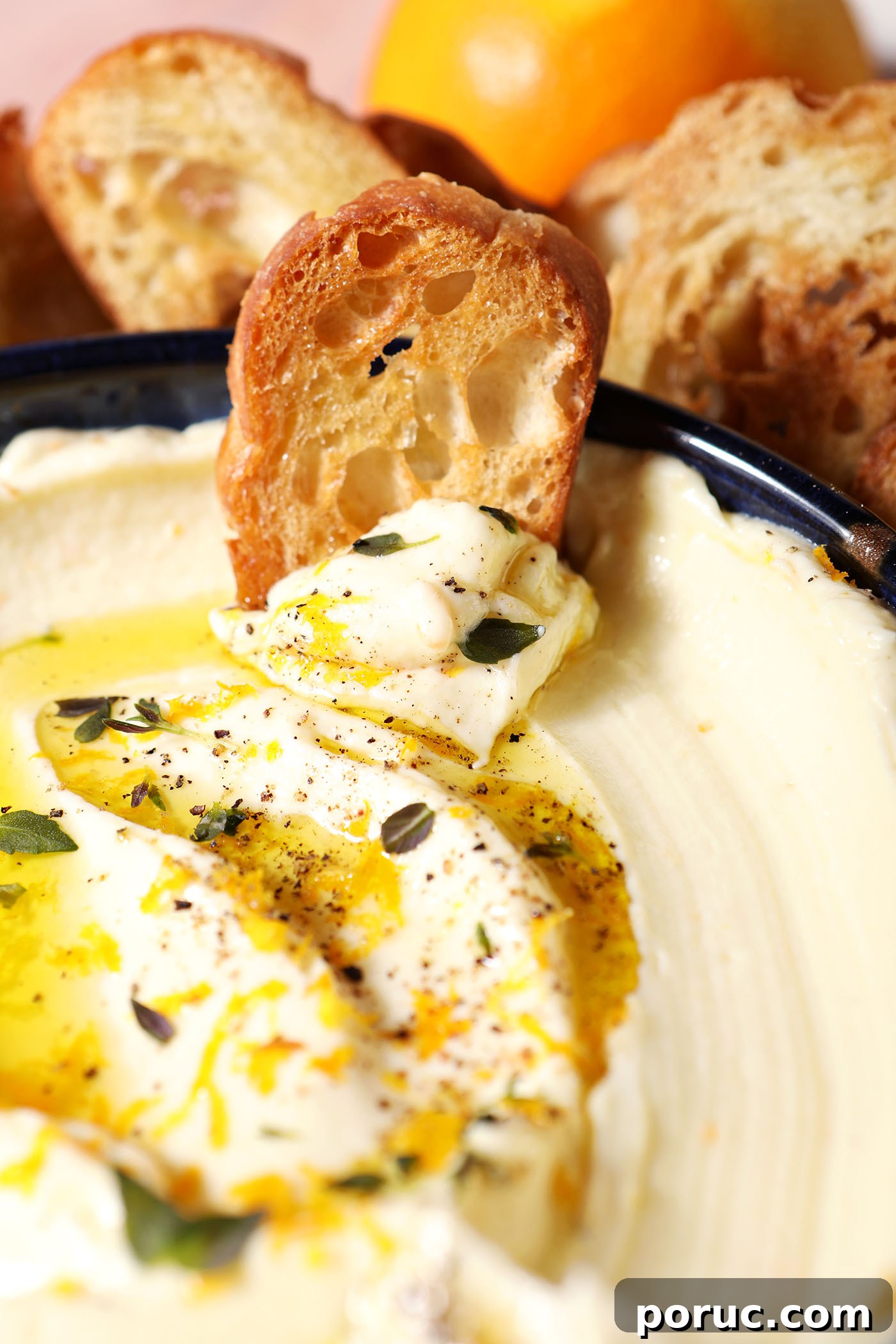 Creamy Whipped Ricotta Dip with Lemon and Herbs 8 A crostini sits on top of a bowl of whipped ricotta garnished with oil, herbs and orange zest