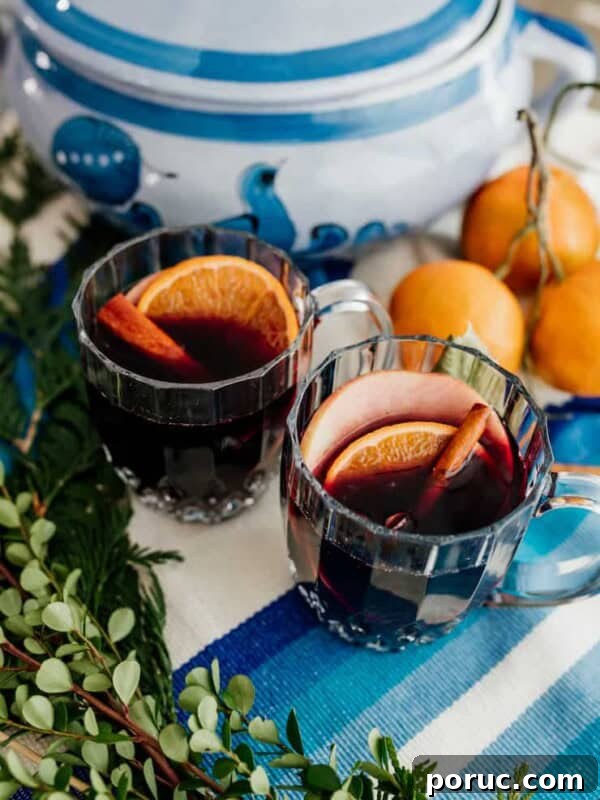 Warm mulled wine served in clear glass mugs on a blue and white holiday tablescape with cinnamon and citrus.