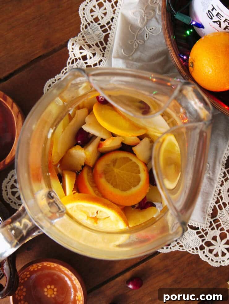 Overhead view looking into a clear glass pitcher with fully muddled fruit, ready for making Christmas sangria.