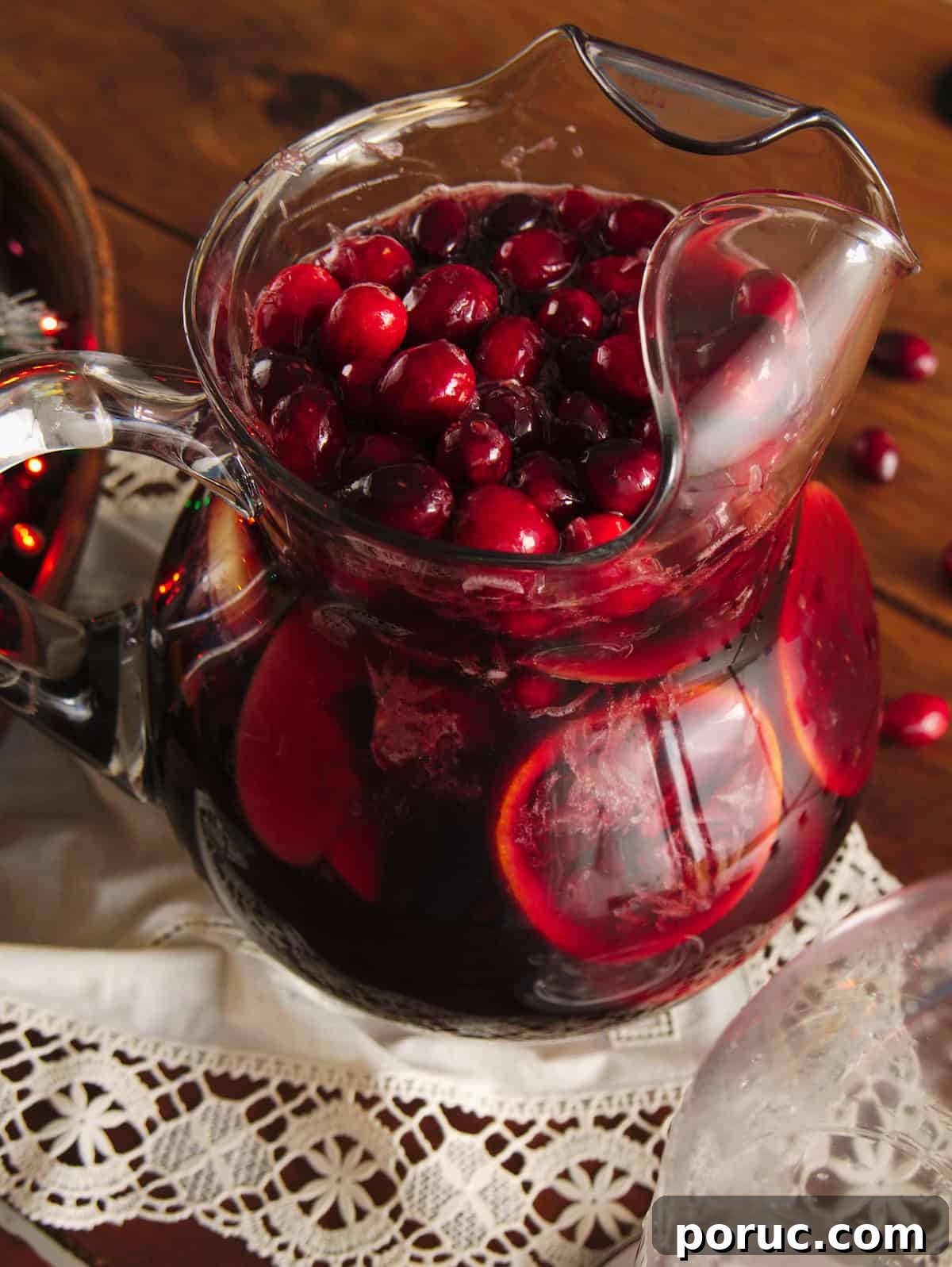 Finished red Christmas sangria after adding club soda, shown at an angle with cranberries floating to the top of the pitcher.