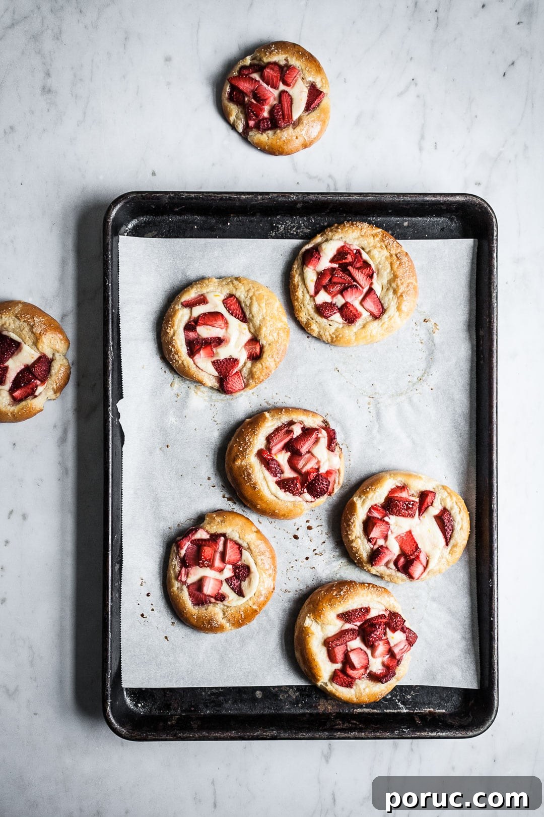 Strawberry Cream Cheese Brioche with Orange Blossom Water 2 Brioche pastries on a black pan with white parchment resting on a marble background