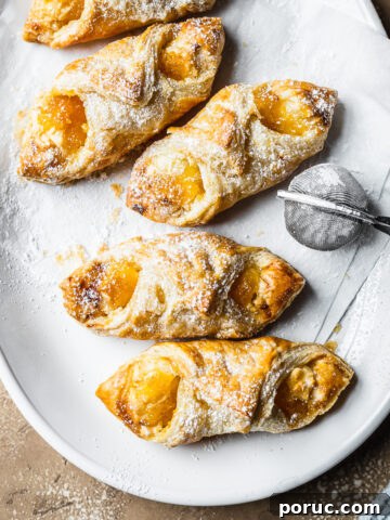 Baked pastries on white parchment on a white ceramic plate. A small metal sieve of powdered sugar rests on the right of the plate.