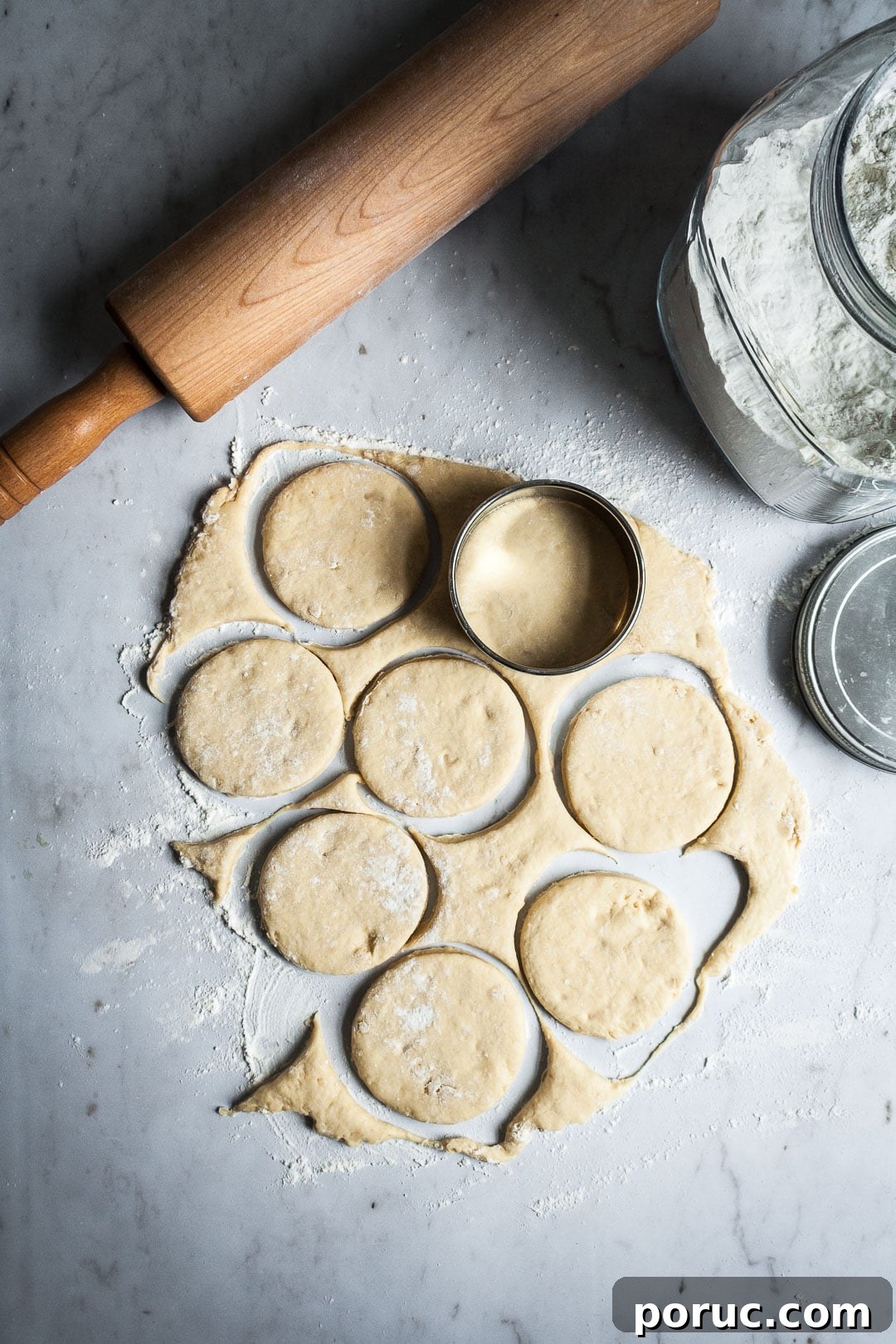 Strawberry Cream Cheese Brioche with Orange Blossom Water 4 Brioche dough being rolled out and cut with a round cutter on a marble surface with rolling pin and flour container nearby
