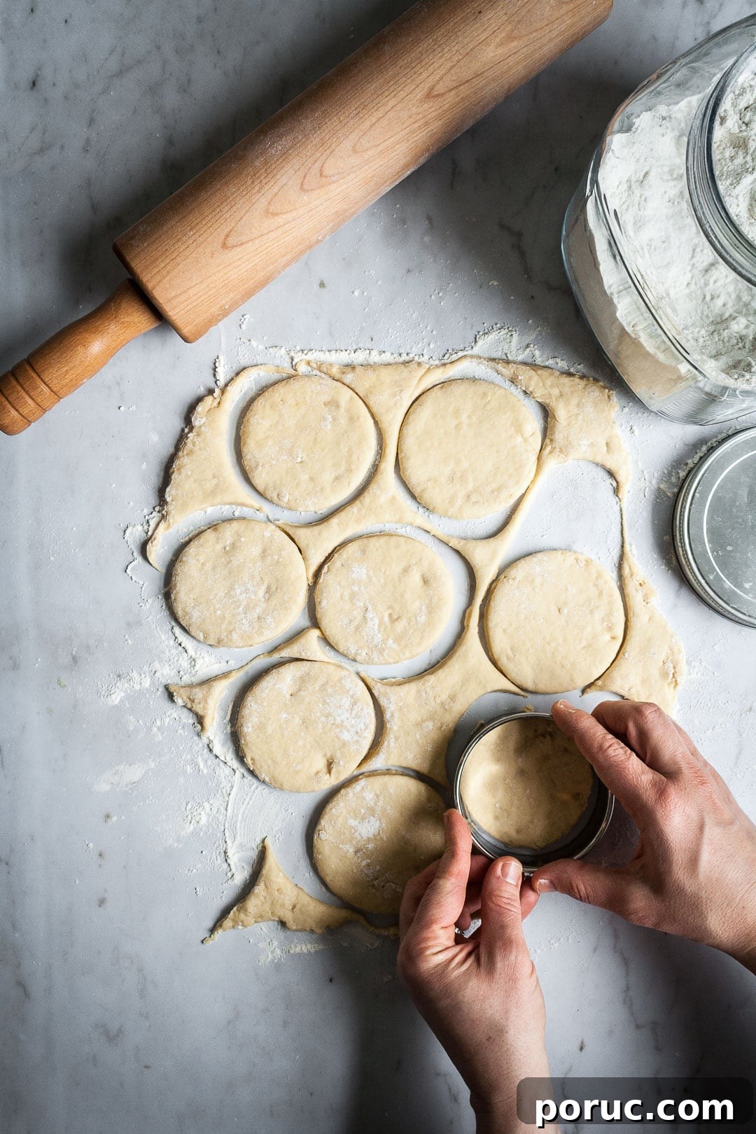 Strawberry Cream Cheese Brioche with Orange Blossom Water 5 Hands cutting rolled out brioche dough into circles, holding a round cookie cutter. All on a marble slab with rolling pin and flour container nearby