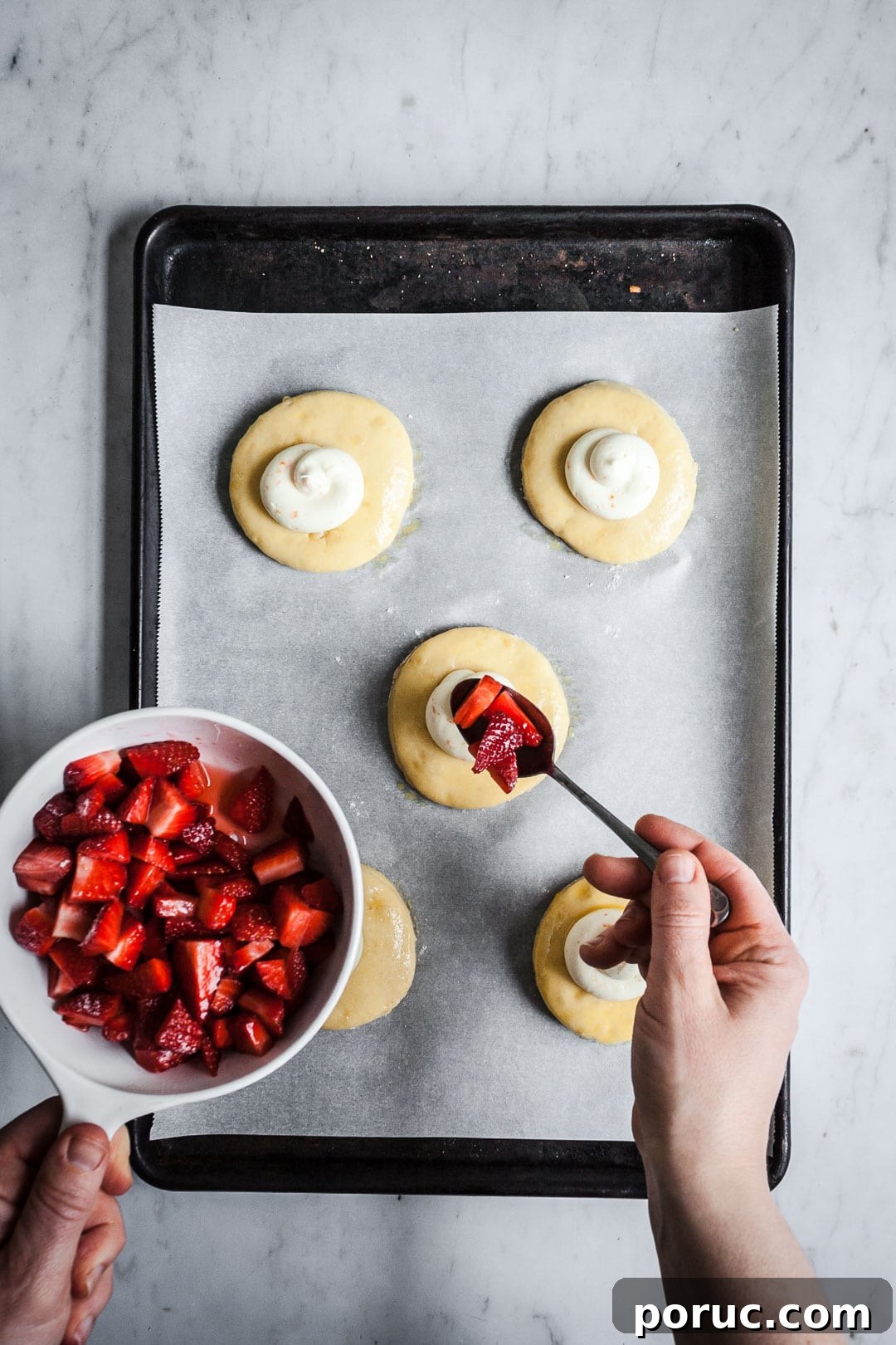 Strawberry Cream Cheese Brioche with Orange Blossom Water 7 Process shot showing hands holding bowl of strawberries, spooning them onto the top of cream cheese brioche pastries