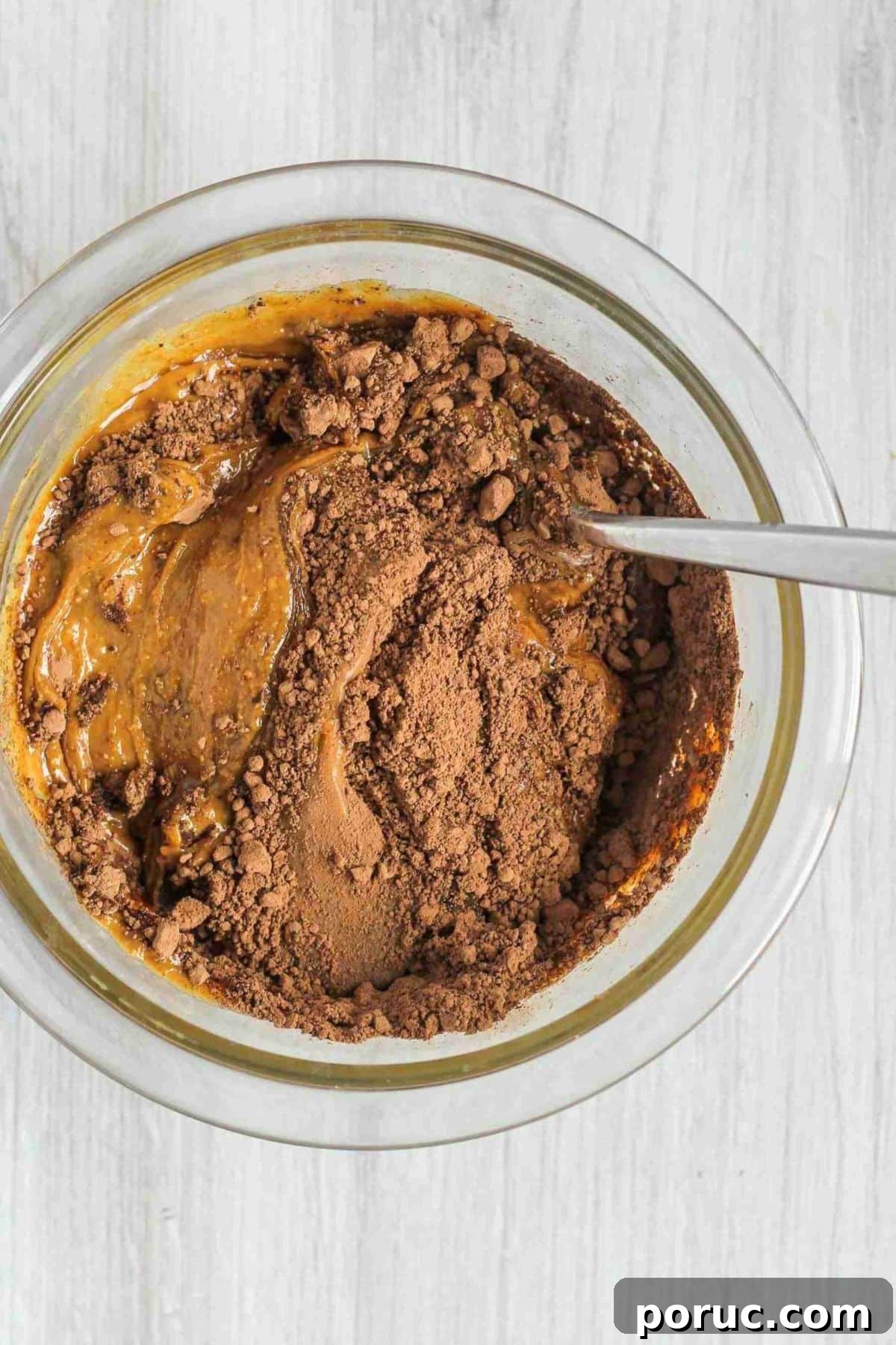 Chocolate Coconut Peanut Butter Energy Bites for Snacks 3 Peanut butter, honey, and cacao being mixed together in a glass mixing bowl.