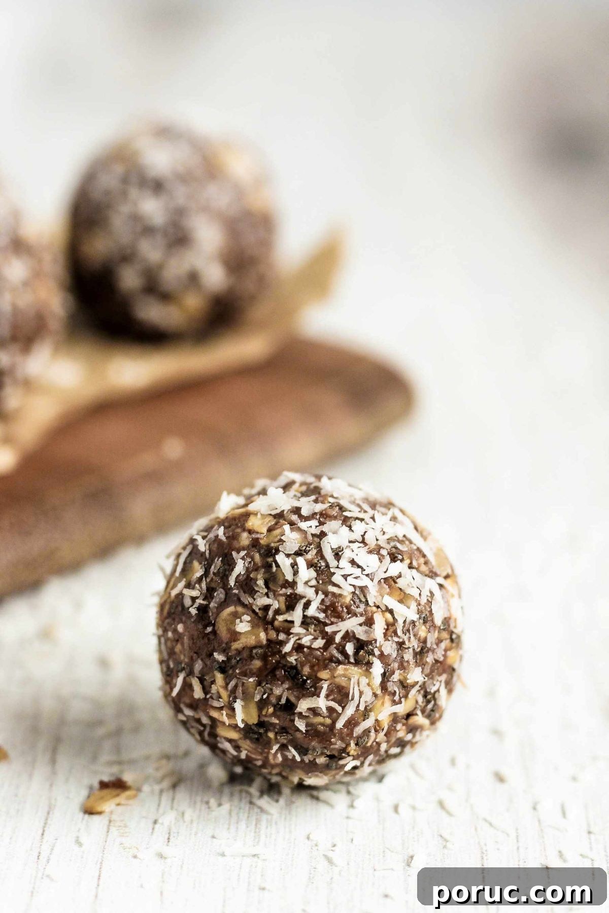 Chocolate Coconut Peanut Butter Energy Bites for Snacks 9 Single peanut butter chocolate coconut ball on a white board with more snack balls in the background.