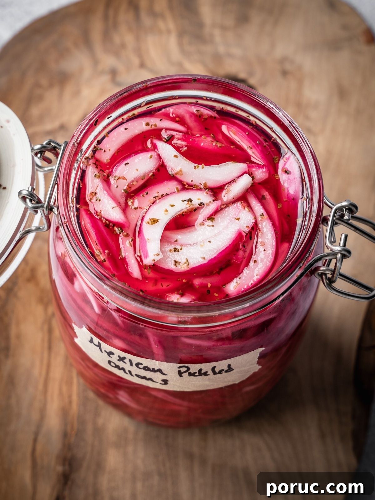 Yucatan-Style Mexican Pickled Red Onions for Tacos & Salads 2 An opened jar of pickled Mexican onions with a label on a wooden board.