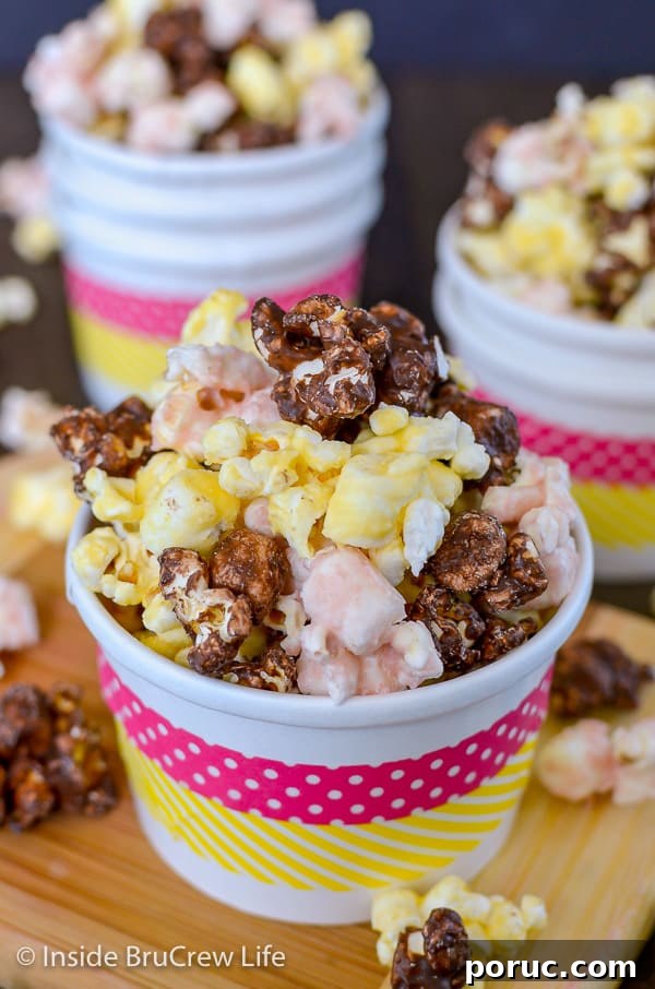Banana Split Popcorn - chocolate, strawberry, and banana flavors give this easy chocolate covered popcorn a fun twist. Great no bake recipe to make for movie nights! A white paper cup with pink and yellow stripes filled with banana split popcorn with more bowls behind it