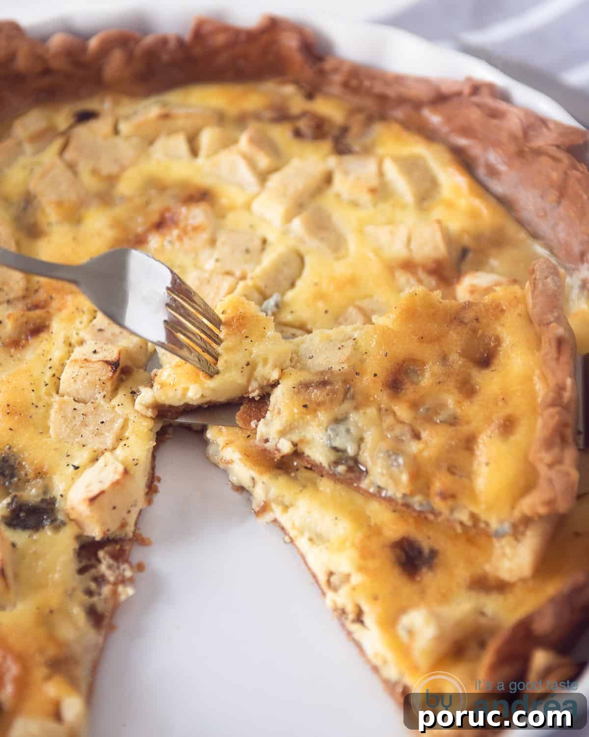 Gorgonzola and Apple Quiche Recipe for Savory Brunch 2 A height photo with an apple gorgonzola quiche from which a point has been cut that lies on top of it. A fork takes a bite of the quiche tip.