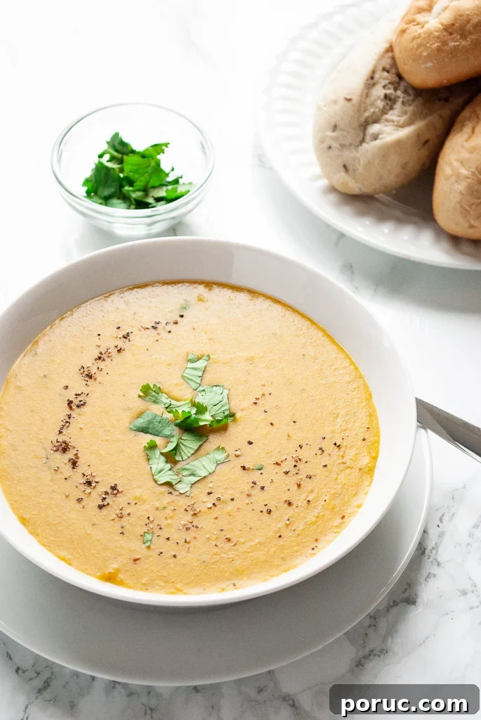 A bowl of moroccan red lentil soup on a table next to a plate of rolls.