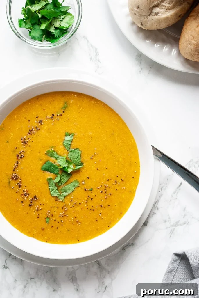 a bowl of moroccan red lentil soup next to a plate of rolls