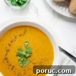 a bowl of moroccan lentil soup on a table alongside a plate of rolls