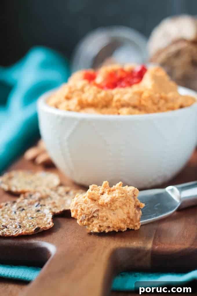 Smoked Almond Cheddar Spread - a delicious and super easy vegan cheddar cheese spread. Only 5 ingredients and made all in the food processor. Spread it on crackers, use it as a sandwich spread, dip fresh fruits and veggies in it - you're gonna love this smoky spread! Metal cheese spreader with vegan cheddar cheese spread. Bowl of cheese spread in the background.
