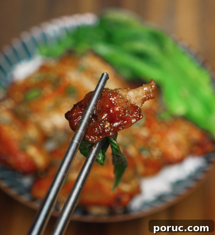 Korean Chicken Bulgogi Recipe: Sweet-Spicy Grilled Chicken 3 Glazed piece of chicken bulgogi held by chopsticks with rice and greens blurred in the background.