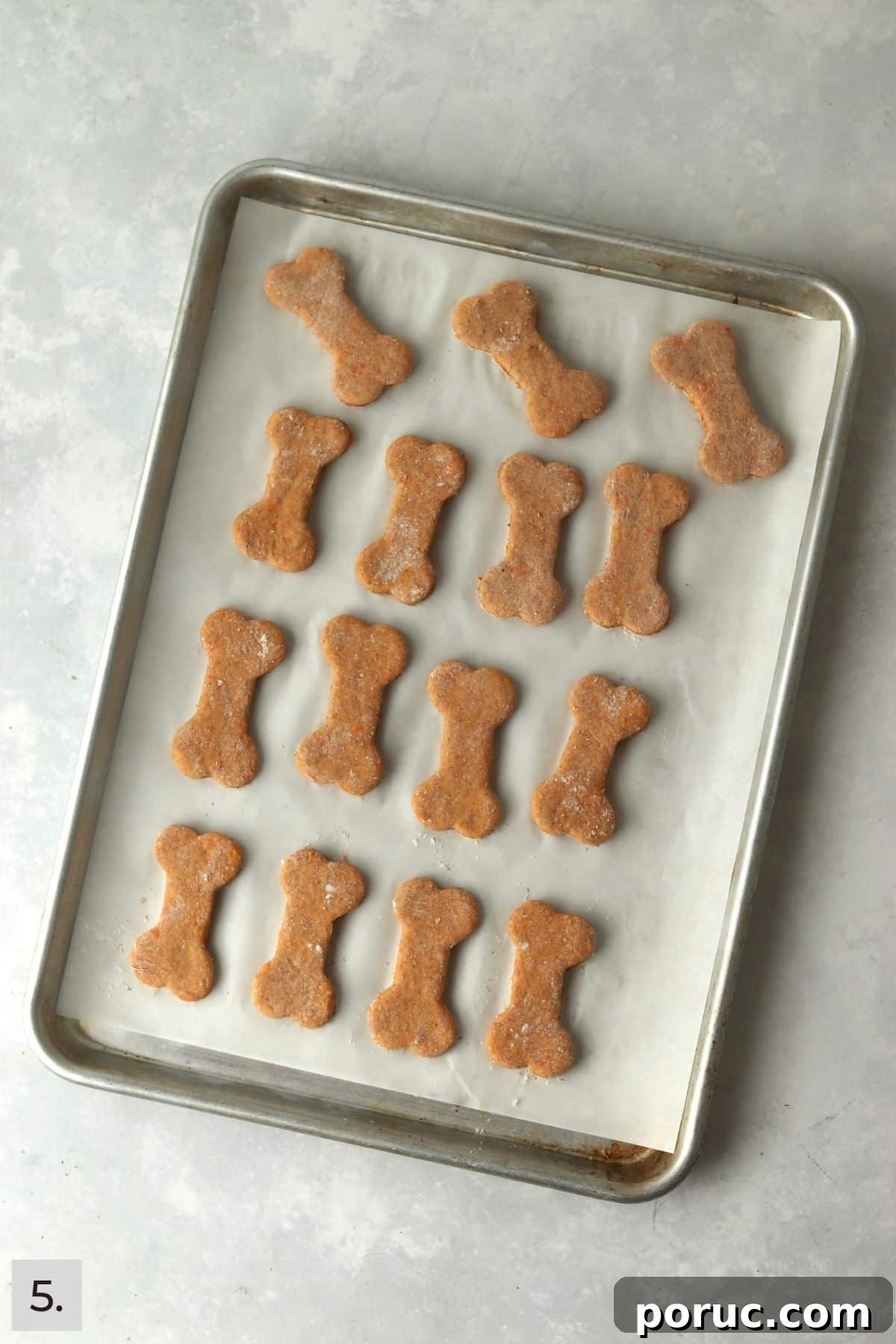 Baked Sweet Potato Dog Treats You Can Make at Home 8 Unbaked sweet potato dog treats cut into bone shapes on a baking sheet.
