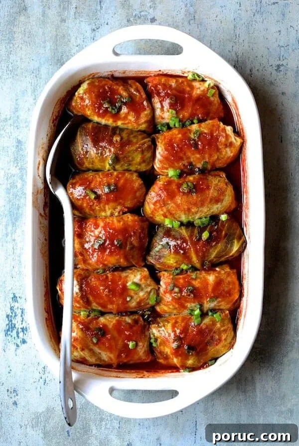 Spicy Asian Pork Cabbage Rolls in white baking dish with white serving spoon after being baked.