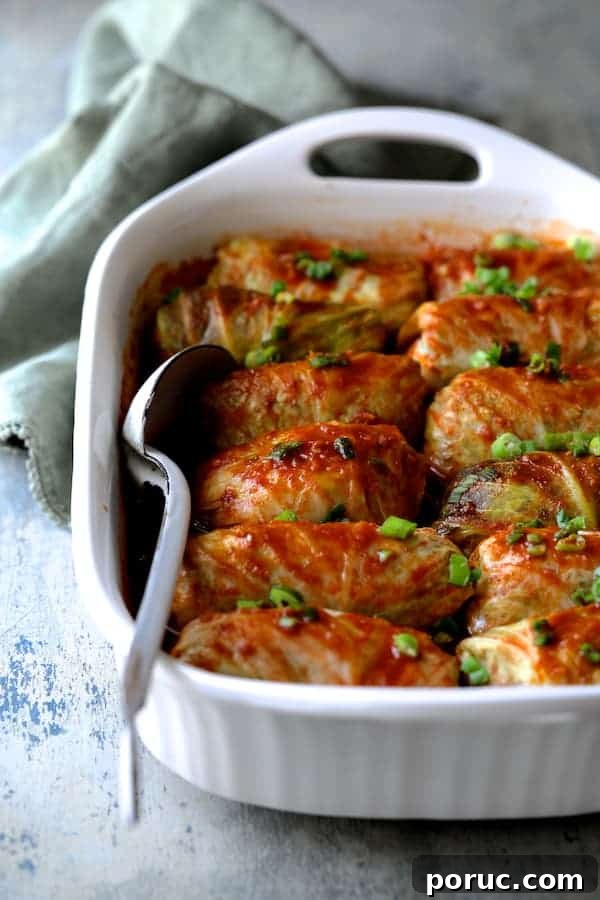 Spicy Asian Pork and Cabbage Rolls with Ginger-Soy Glaze 7 Photo of cooked Spicy Asian Pork Cabbage Rolls in white baking dish on blue background with green dish towel and white metal spoon.