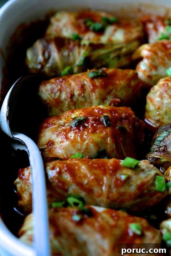 Spicy Asian Pork and Cabbage Rolls with Ginger-Soy Glaze 8 Close-up photo of Spicy Asian Pork Cabbage Rolls in white baking dish with white metal spoon.