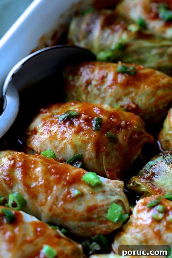 Spicy Asian Pork and Cabbage Rolls with Ginger-Soy Glaze 9 Close-up photo of cooked Spicy Asian Pork Cabbage Rolls in white baking dish with white metal spoon.