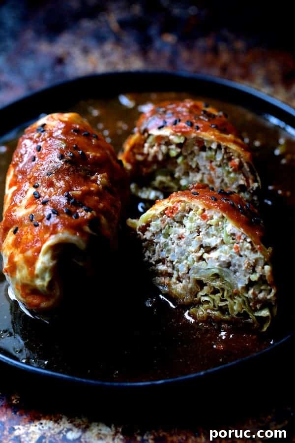 Spicy Asian Pork and Cabbage Rolls with Ginger-Soy Glaze 10 Photo showing Spicy Asian Pork Cabbage Rolls cut in half on black plate garnished with sesame seeds.