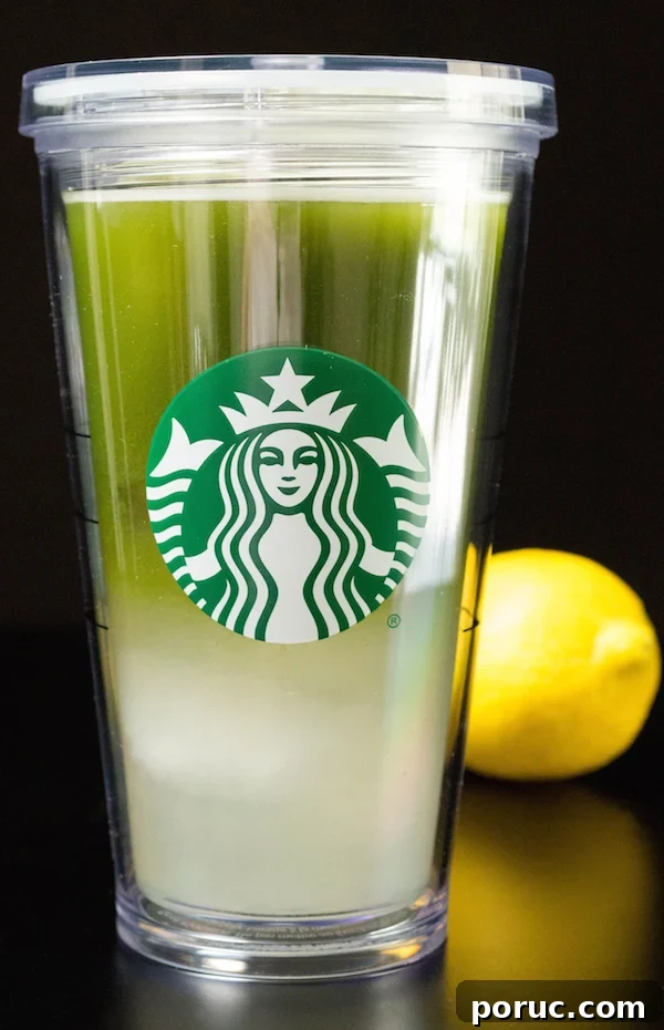 Starbucks-Style Matcha Lemonade Recipe You Can Make at Home 4 A grande starbucks cup filled with matcha lemonade. A lemon sits in the background.