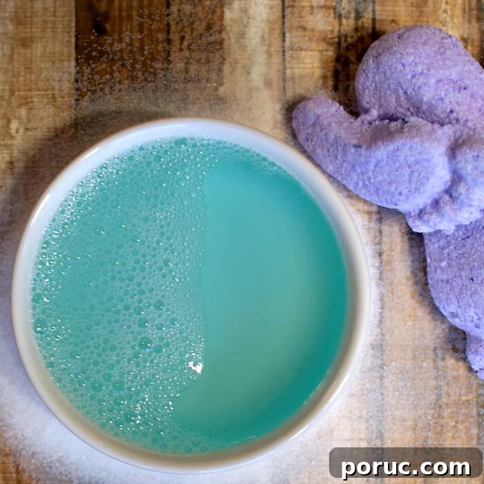 Mamma’s Famous Foot Exfoliation Elixir — Natural Foot Peel Recipe 2 A bowl of vibrant blue foaming liquid next to a purple exfoliating scrub, showcasing a homemade foot exfoliation elixir on a wooden surface.