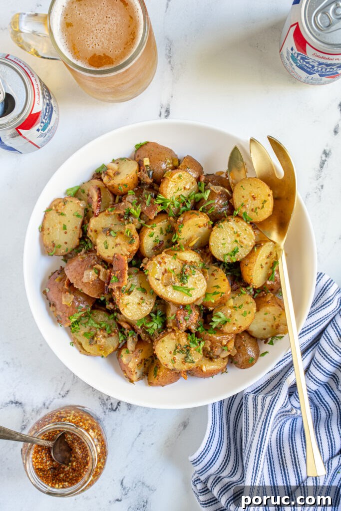 Overhead of a white bowl full of warm German potato salad with whole grain mustard, bacon, and fresh parsley. 