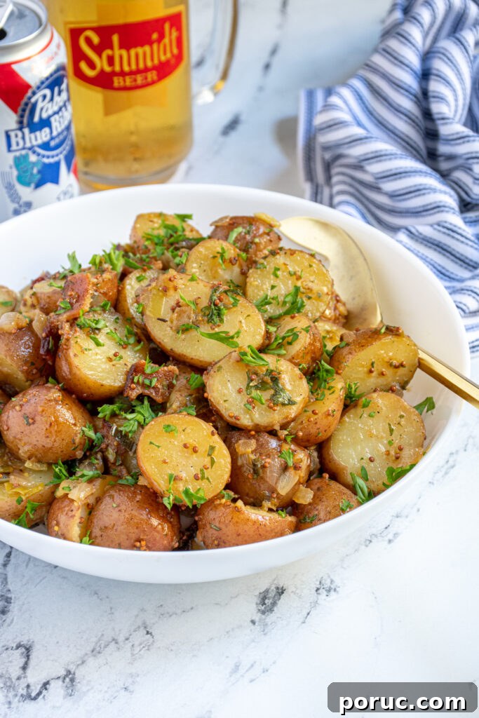 Side view of a large white bowl filled with German potato salad covered in a mustard sauce, with bacon bits and fresh parsley.