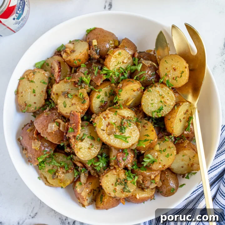A white bowl of German potato salad with a spoon showing off saucy halved potatoes with bacon and fresh parsley.