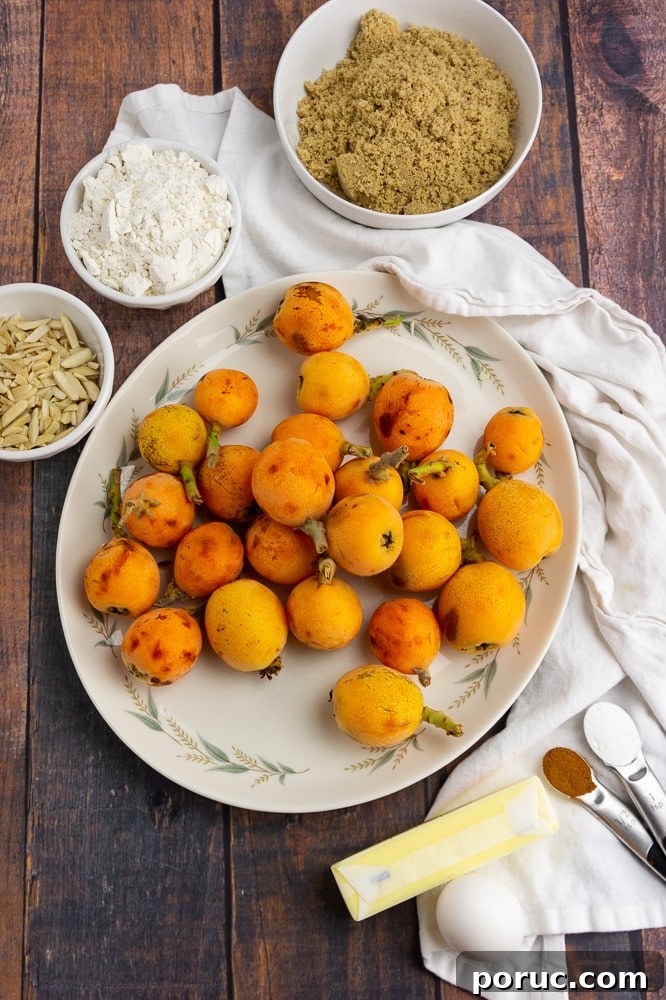 Warm Loquat Cobbler Recipe with Sweet Biscuit Topping 3 a white platter full of loquats with a bowl of brown sugar, a small bowl of almonds, a small bowl of flour, a stick of butter and a teaspoon of cinnamon on a white towel