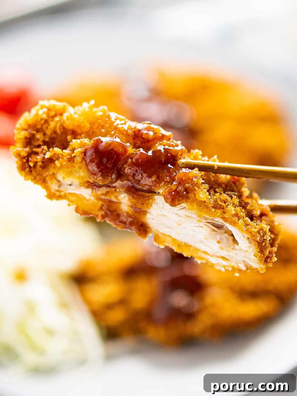Close up of a piece of chicken katsu with katsu sauce held by chopsticks.
