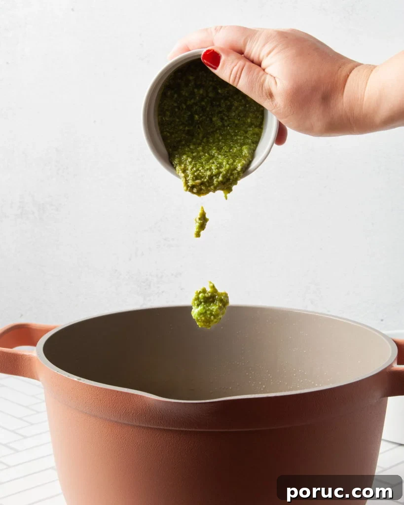 One-Pot Mushroom Pesto Pasta with 4 Ingredients 8 Adding pesto to a large pot with cooked pasta and mushrooms.