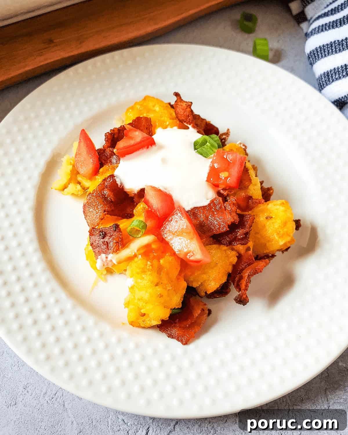 Cheesy Bacon Loaded Tater Tots Recipe 7 A plate with bacon, tomatoes and sour cream, loaded with tater tots.