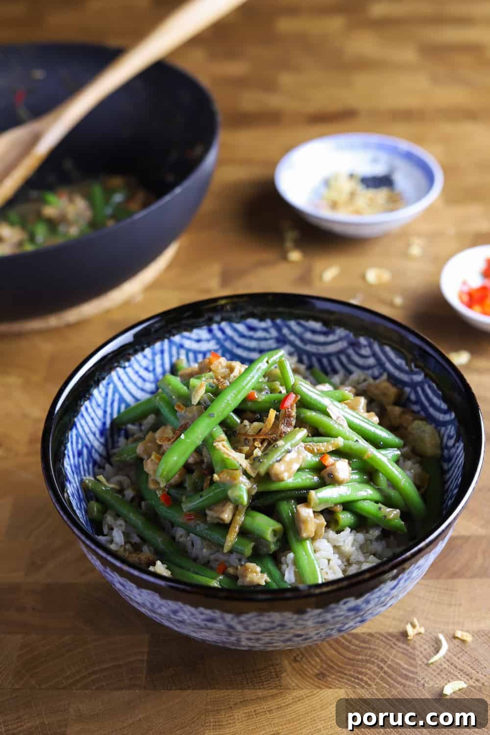 Chinese-Style Green Beans with Crispy Tempeh (Vegan Recipe) 4 Photo of a bowl of vegan chinese green beans with tempeh and pan in the background