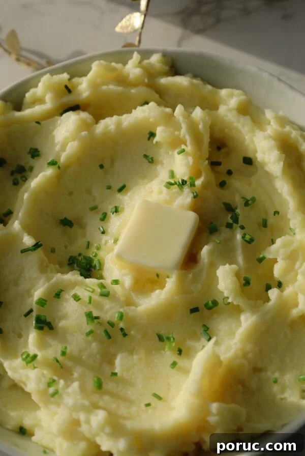 Garlic mashed potato recipe in a large bowl with butter and chives.