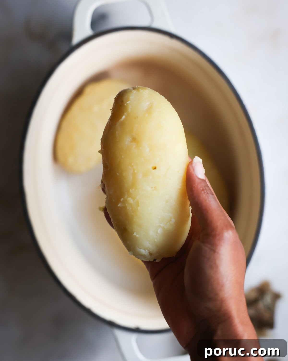 Fluffy Vegan Mashed Potatoes Recipe for Creamy Comfort 8 overhead of a peeled potato in a hand
