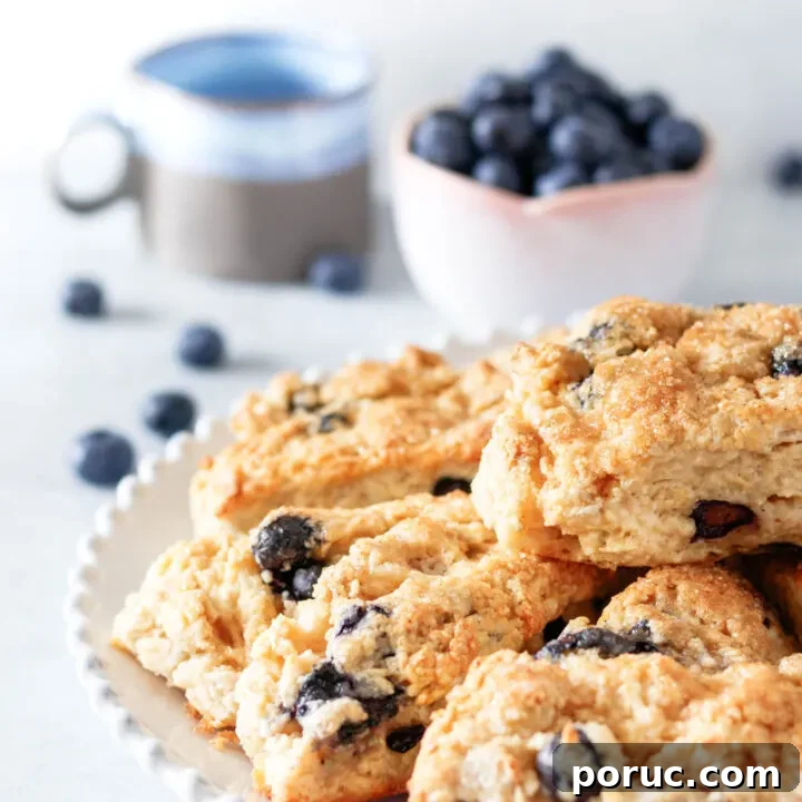 Angled top view of the scones piled on a plate with fresh blueberries and a grey and blue glazed coffee cup in the background