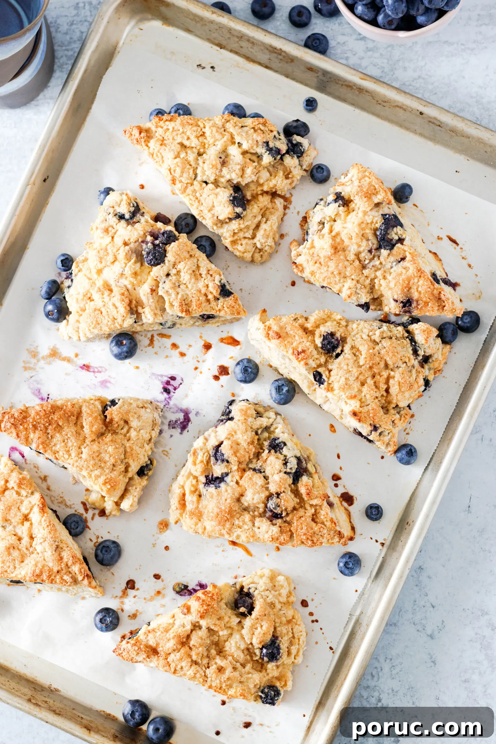 Tender Fluffy Blueberry Scones Recipe — Step-by-Step Guide 5 Top view of the baked scones on a light aluminum rimmed baking sheet with scattered blueberries